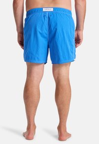 Men's blue swim shorts in lightweight fabric with an elastic waistband and white stitching detail, ending above the knee.