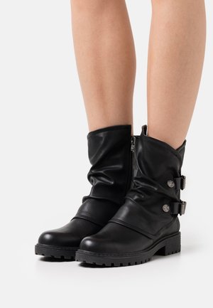 Bottes à la cheville en cuir noir à design décontracté, avec fermetures éclair et sangles ornées d'accents métalliques, et semelles en caoutchouc texturé.