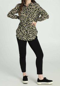 Camicia a maniche lunghe con bottoni, stampa leopardata nera e verde, abbinata a pantaloni neri aderenti e sneakers nere con suola bianca.