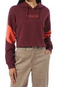 Tyrkysová zkrácená mikina s oranžovými akcenty. Disponuje kapucí na šňůrku a logem "VANS" v kontrastní barvě. Spárována s béžovými kalhotami.