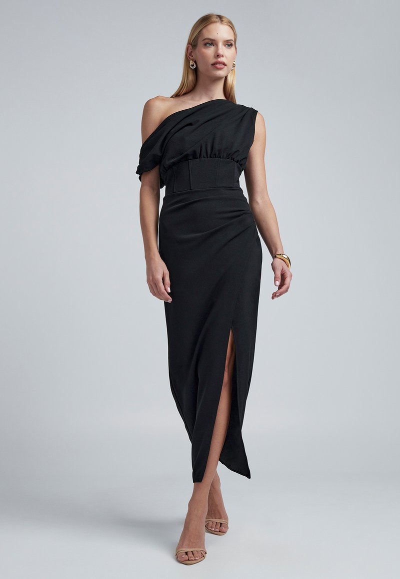 Mustast asümmeetrilisest riidest kleit ühe õlaga, taljesse tõmmatud ja esiosas lõhikuga. Sile tekstuur ja voolav disain. Kaunistatud peente voldikute lisanditega.