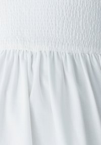 Robe blanche avec un buste texturé et smocké et une jupe fluide et froncée. Tissu léger avec une finition mate douce. Design simple et cohérent.