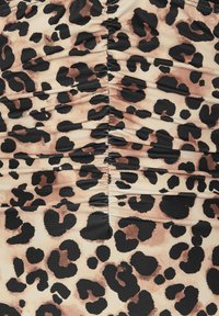 Le tissu à imprimé léopard présente des nuances variées de beige, de marron et de noir. La texture froncée court verticalement, rehaussant la profondeur du design.