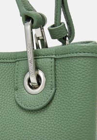 Zielona torebka z teksturowanej skóry z srebrnym okuciem, z okrągłym oczkiem i zapięciem. Gładki pasek do noszenia.