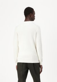 Maglione bianco a coste con scollo rotondo, maniche lunghe e vestibilità morbida, abbinato a pantaloni verde scuro.