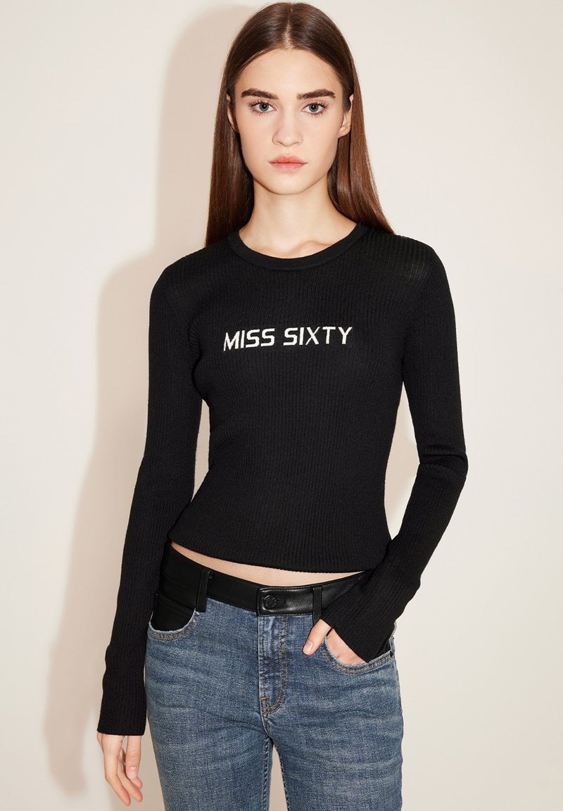 Schwarzes, geripptes Langarmoberteil mit dem aufgestickten Schriftzug "MISS SIXTY" in Weiß, kombiniert mit blauen Jeans und einem schwarzen Gürtel.