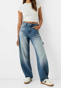 Breda blå jeans i denim med ljus tvätt, hög midja och fem fickor, matchade med vita sneakers och en tajt vit topp.