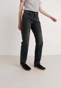 Jeans negros de cintura alta con corte recto, con un ligero desgaste, cinco bolsillos y un cierre clásico de cinco botones.