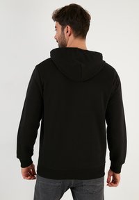 Felpa nera con cappuccio regolabile, polsini e orlo a costine. Tessuto morbido in misto cotone con un design semplice. Nessun logo o motivo visibile.