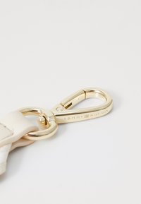 Chiusura in metallo dorato con una cintura in pelle crema texture, con il marchio "TOMMY HILFIGER" inciso sull'hardware.