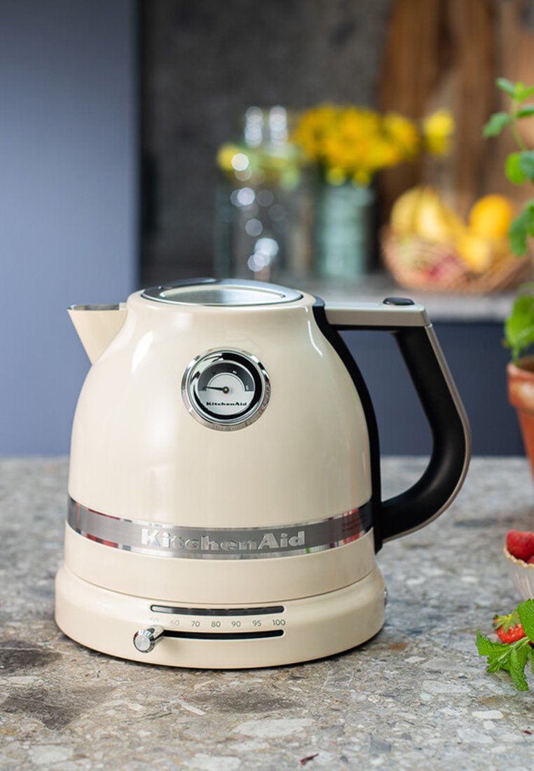 Krämfarbener KitchenAid-Wasserkocher mit einem Edelstahlring, runder Form, schwarzem Griff und Temperaturanzeige auf der Vorderseite.