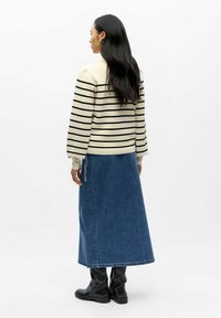 Maglione a righe color crema con maniche a sbuffo, abbinato a una lunga gonna di jeans blu e stivali neri in pelle alla caviglia. Texture liscia, design casual.