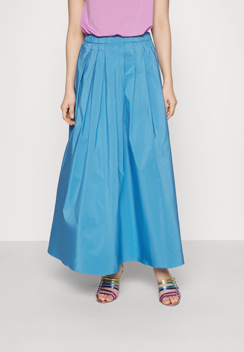 Jupe longue plissée bleu clair avec une ceinture élastique, associée à des sandales multicolores à brides. Texture lisse, longueur chevilles.
