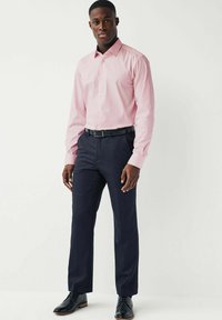Helles pinkes Langarmhemd mit Button-Down-Kragen, kombiniert mit dunklen marineblauen Hosen und schwarzen Schuhen, in schlanker Passform und mit feiner Struktur.