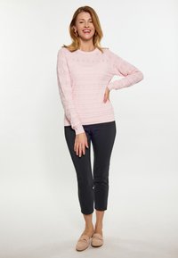 Maglione lavorato a maglia rosa chiaro con motivi testurizzati, abbinato a pantaloni cropped neri e mocassini beige morbidi.