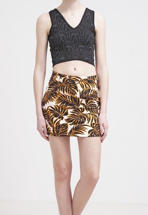 Sort cropped top med tekstureret bladmønster, parret med en tætsiddende hvid nederdel med stort brunt og orange tropisk bladmønster.