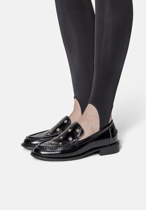 Mocassins en cuir verni noir avec un design à enfiler, des clous ronds proéminents sur le dessus et un talon bas carré.