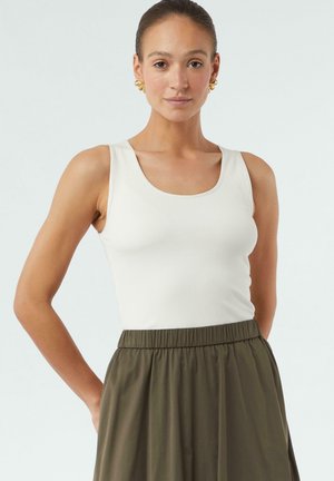 White ribbed tank top with a scoop neckline, paired with an olive-green high-waisted skirt featuring an elastic waistband.