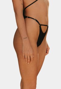 Czarne majtki bikini o minimalnym wykończeniu, z cienkimi regulowanymi ramiączkami i okrągłymi akcentami z metalu. Gładka tekstura materiału.