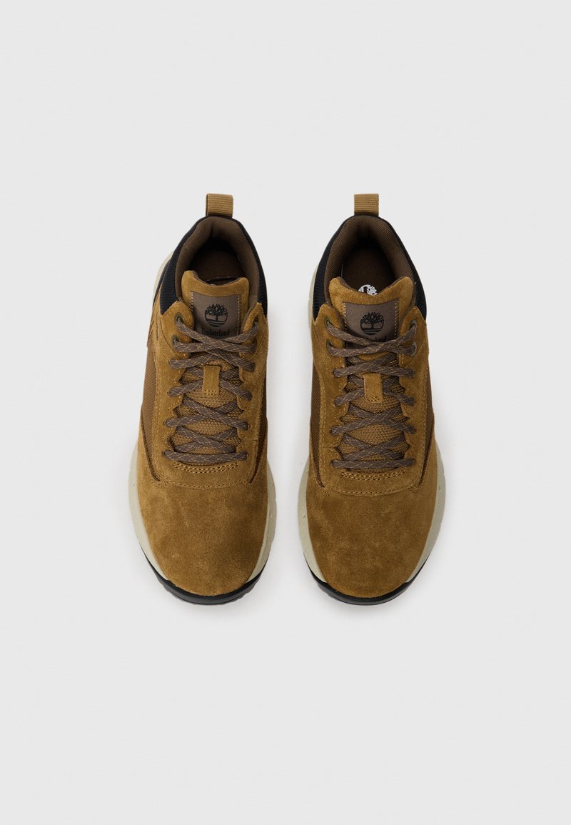 Zapatillas de ante marrón con un cuello textil negro, cordones planos y una suela acolchada. Presentan un parche con el logo en la lengüeta.