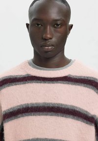 Roze gestreepte trui gemaakt van zacht gebreid materiaal met donkergrijze en bordeauxrode horizontale strepen. Klassieke ronde hals, ontspannen pasvorm.
