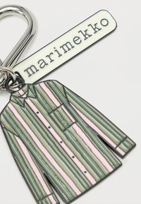 Μπρελόκ με ριγέ μακρυμάνικο πουκάμισο σε πράσινο και ροζ σμάλτο και μια λευκή ετικέτα με την ένδειξη «marimekko» που είναι προσαρτημένη σε μεταλλικό δαχτυλίδι.