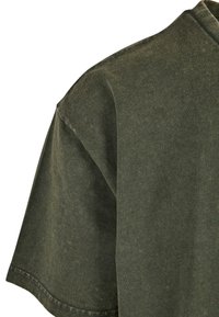 Tmavo zelené bavlnené tričko s krátkymi rukávmi, s okrúhlym výstrihom a jemne textúrovanou látkou. Obsahuje viditeľný šev na leme.