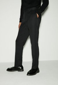 Schwarze maßgeschneiderte Hosen mit geradem Schnitt, strukturiertem Stoff, seitlichen Taschen und einem glatten Bund, ergänzt durch schwarze Lederschuhe.