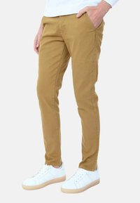 Chinos in cotone beige con una vestibilità slim, dotati di tasche laterali e una texture liscia, abbinati a sneakers bianche con suola in gomma.