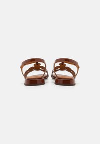 Sandales en cuir verni marron avec un dos ouvert, un design découpé décoratif, une semelle plate et une bride de cheville. Texture lisse avec une finition brillante.