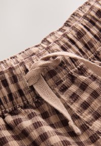 Gros plan sur un pantalon beige et marron à carreaux avec une taille élastique et un cordon tressé noué.