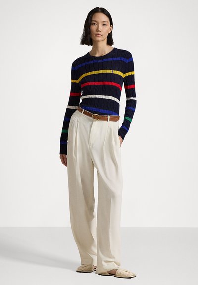 Suéter de malha canelada azul-marinho com riscas horizontais multicoloridas, combinado com calças largas plissadas em creme e um cinto castanho.