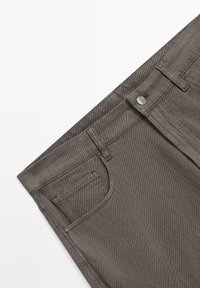 Graue Denim-Jeans mit einer horizontal gerippten Struktur, ausgestattet mit einem Reißverschluss, vorderen Taschen und einer silberfarbenen Knopfverzierung.