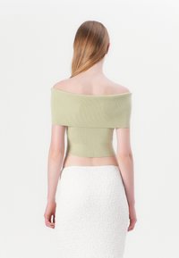 Top corto sin hombros de tela acanalada en verde claro, diseño ajustado. Usado con una falda blanca texturizada, visto desde la espalda.