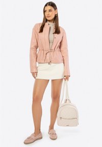 Giacca di pelle rosa con vita regolabile, top beige, mini gonna bianca, mocassini rosa e uno zaino beige trapuntato.