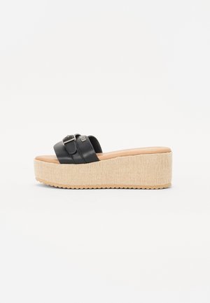 Sandalias de plataforma de cuero negro con una tira ancha y detalle de hebilla. Presenta una base texturada color beige similar al yute y una suela de goma estriada.