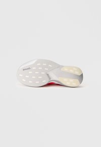Semelle de chaussure avec une finition argentée texturée, dotée d'accents en caoutchouc blanc et d'un motif de crampons circulaires pour une meilleure adhérence et durabilité.