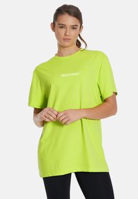 Ljusgrön, kortärmad t-shirt i mjukt tyg, med texten "SQUATPROOF" i vitt på bröstet. Avslappnad passform med rund halsringning.