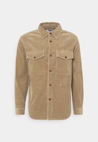 Camisa de pana color camel con cuello abotonado, dos bolsillos en el pecho y botones marrones. Presenta una textura acanalada vertical y mangas largas.