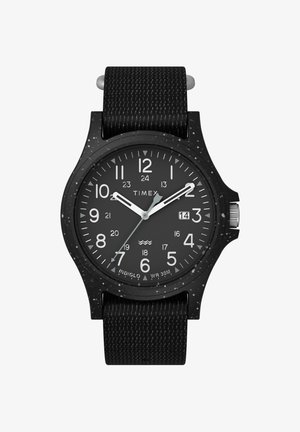 Montre Timex noire avec un boîtier rond, des marquages horaires blancs et un affichage de la date. Caractéristiques d'un bracelet noir texturé et d'accents en matériel argenté.