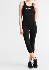 Canotta sportiva nera e leggings capri, entrambi con i loghi Nike swoosh bianchi. Il materiale sembra liscio e compressivo, progettato per l'abbigliamento sportivo.
