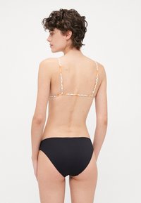 Svart bikinitruse kombinert med en mønstret bralette med tynne stropper. Braletten har et design i oransje og hvitt.