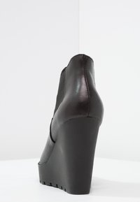 Bota de cuña negra para el tobillo con parte superior de cuero liso, paneles laterales elásticos y una suela de goma gruesa con ranuras con patrón.