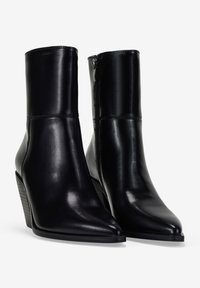 Botines de cuero negro con punta afilada, tacón en cuña y cremallera lateral. La textura suave y el diseño elegante acentúan el estilo moderno.