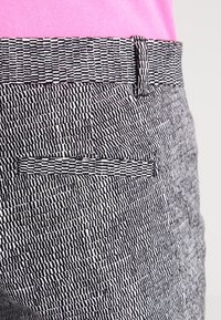 Black and white patterned trousers with a textured finish, featuring a matching belt and a single back pocket.