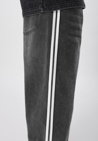 Γκρι τζιν παντελόνι με ίσια κοπή, με δύο κάθετες λευκές ρίγες κατά μήκος της εξωτερικής ραφής και λεπτομέρεια πίσω τσέπης.