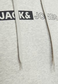 Világosszürke kapucnis felső fekete "JACK & JONES" logóval. Húzózsinórral rendelkezik, amely szövött textúrájú. Puha anyag, laza design.
