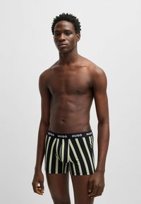 Schwarz-grün gestreifte Boxershorts mit einem weichen elastischen Bund, auf dem der Markenname "HUGO" prominent angezeigt wird.