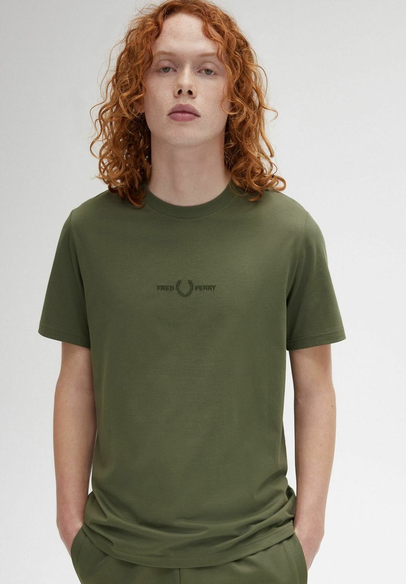 Camiseta de algodón color verde oliva con cuello redondo, mangas cortas y logotipo bordado de "Fred Perry" en verde oscuro, centrado en el pecho.