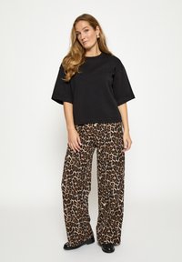 Čierne nadmerné tričko v kombinácii so širokými nohavicami s leopardím vzorom. Oblečenie je vyrobené z jemnej látky a má voľný strih.